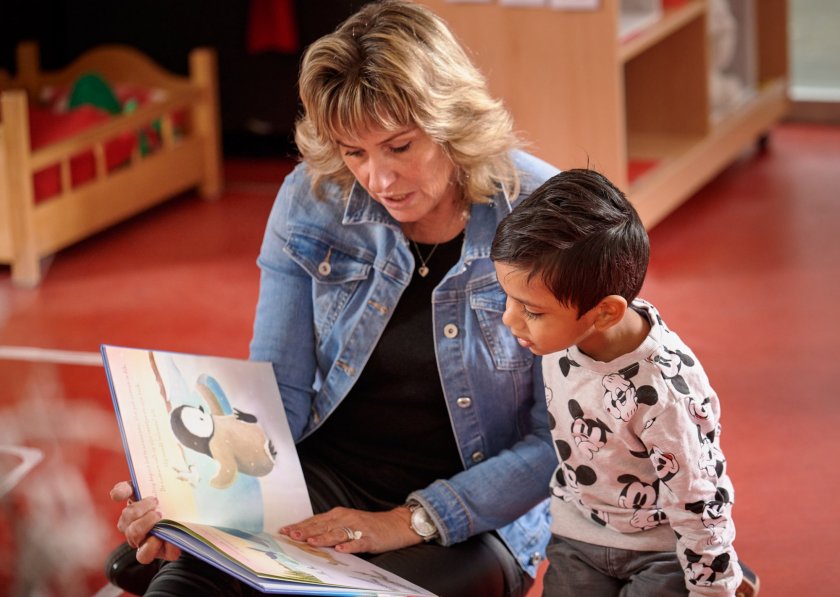 Juf en peuter lezen samen uit een boek.