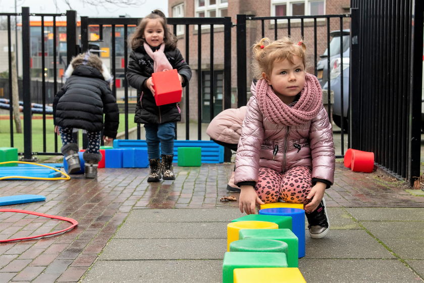 Peuters spelen samen buiten met blokken.